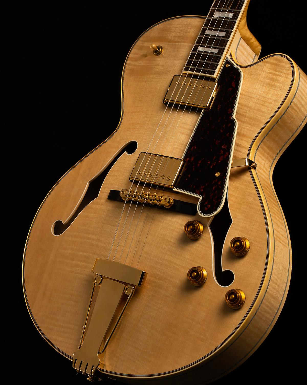 Close-up of an unbranded blonde hand-carved archtop guitar with gold hardware